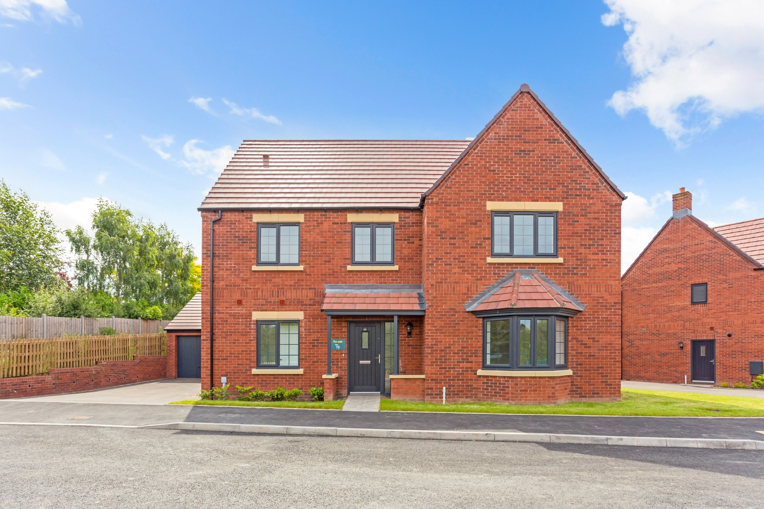 A large red bricked home with bay window, driveway, detached garage and a ample size grassed garden at the front with pathway leading to the front door