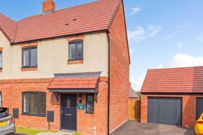 A semi-detached red bricked home with driveway and detached garage