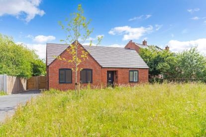 A red bricked bungalow at the end of a long drive with a common grassed area in front