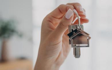 A set of keys with a house keyring behind held up by a hand