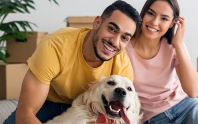 Two people sat with a dog in front of moving boxes 