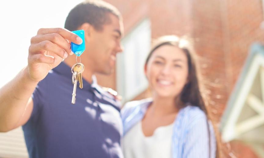 A couple stood outside a house in an embrace holding keys