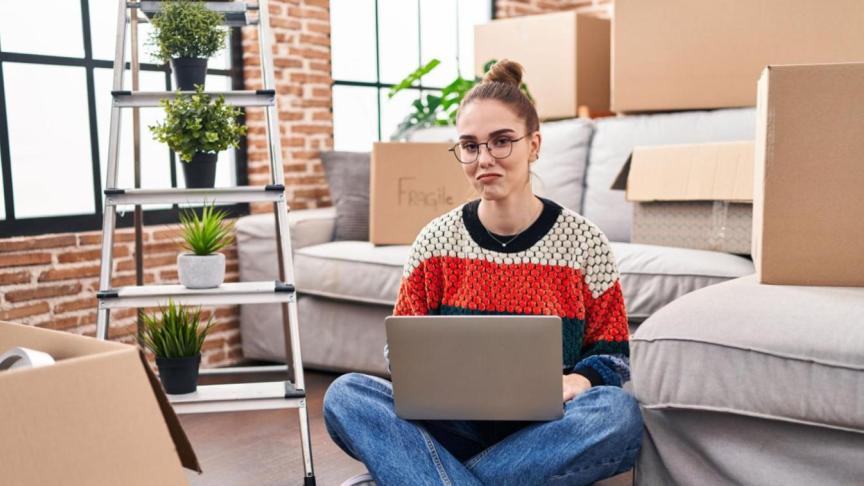 A person sat on the floor of their home after moving in, surrounded by moving boxes.