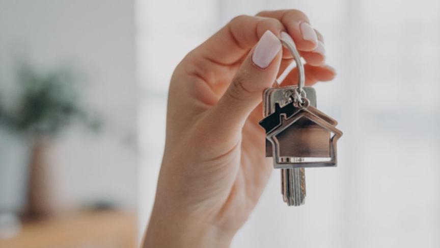 A set of keys with a house keyring behind held up by a hand