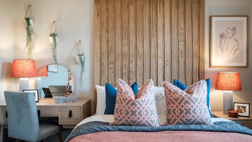 A double bedroom decorated in pastel colours with wooden panelling behind the bed and a desk in the corner
