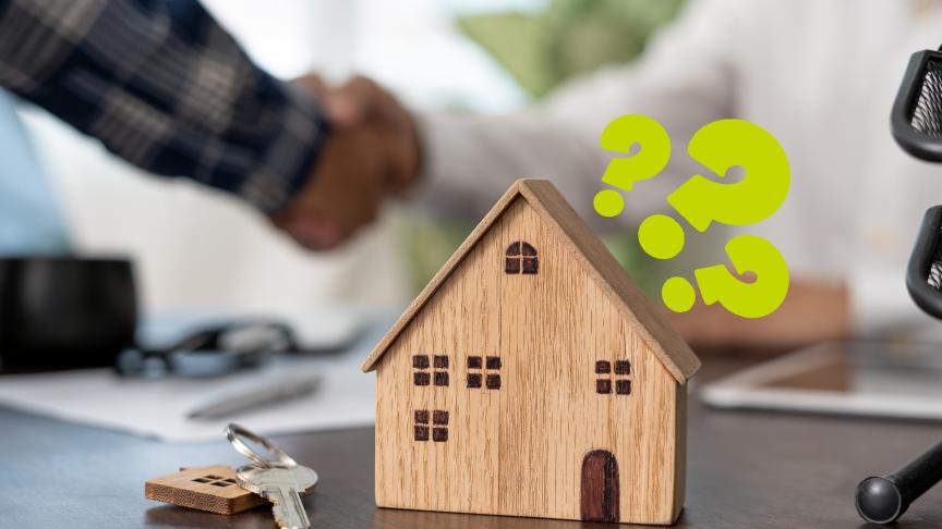 A wooden model of a house on a table next to a keychain with a silver key and a model house keyring on it. There are question marks around the model house and a handshake in the background